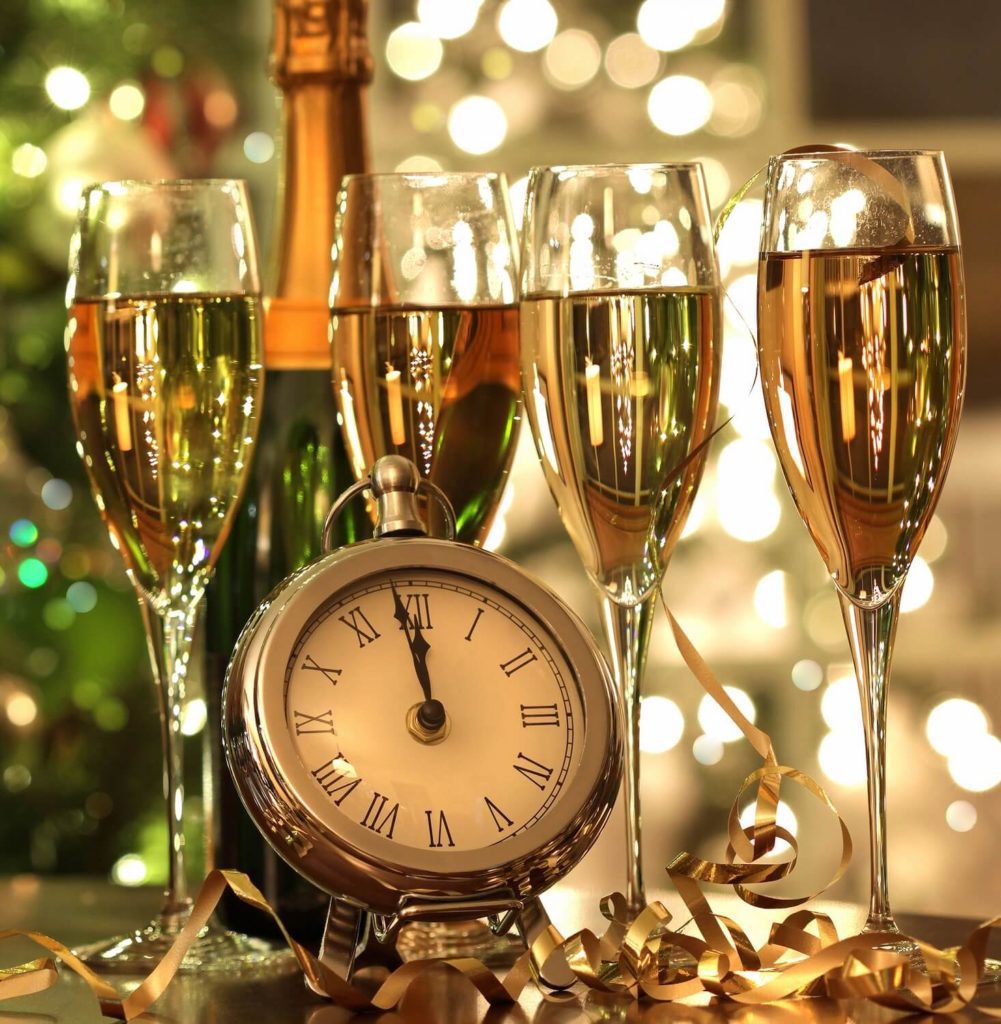 Foto que ilustra matéria sobre decoração de Ano Novo mostra um relógio junto com quatro taças cheias de espumante e uma garrafa atrás.