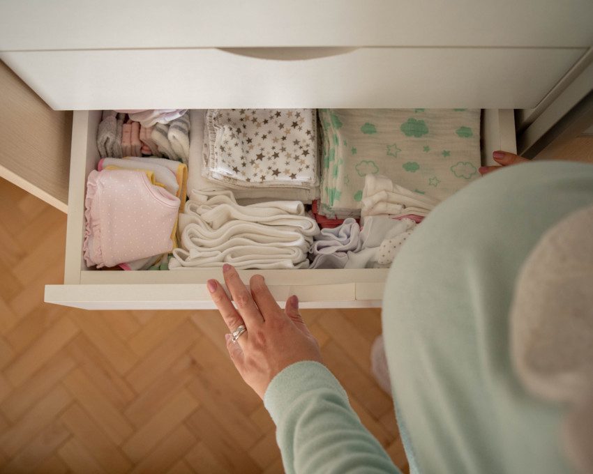 Imagem de uma mulher grávida abrindo uma gaveta da cômoda do bebê.