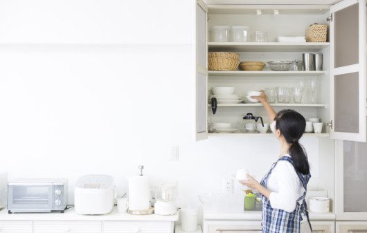 Imagem de uma mulher organizando um armário de cozinha.