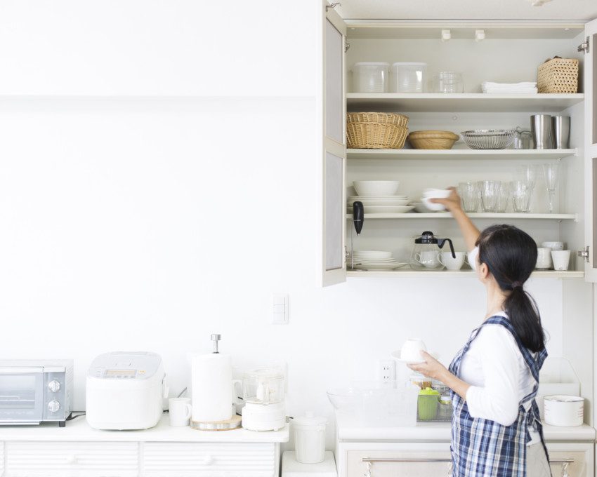 Imagem de uma mulher organizando um armário de cozinha.