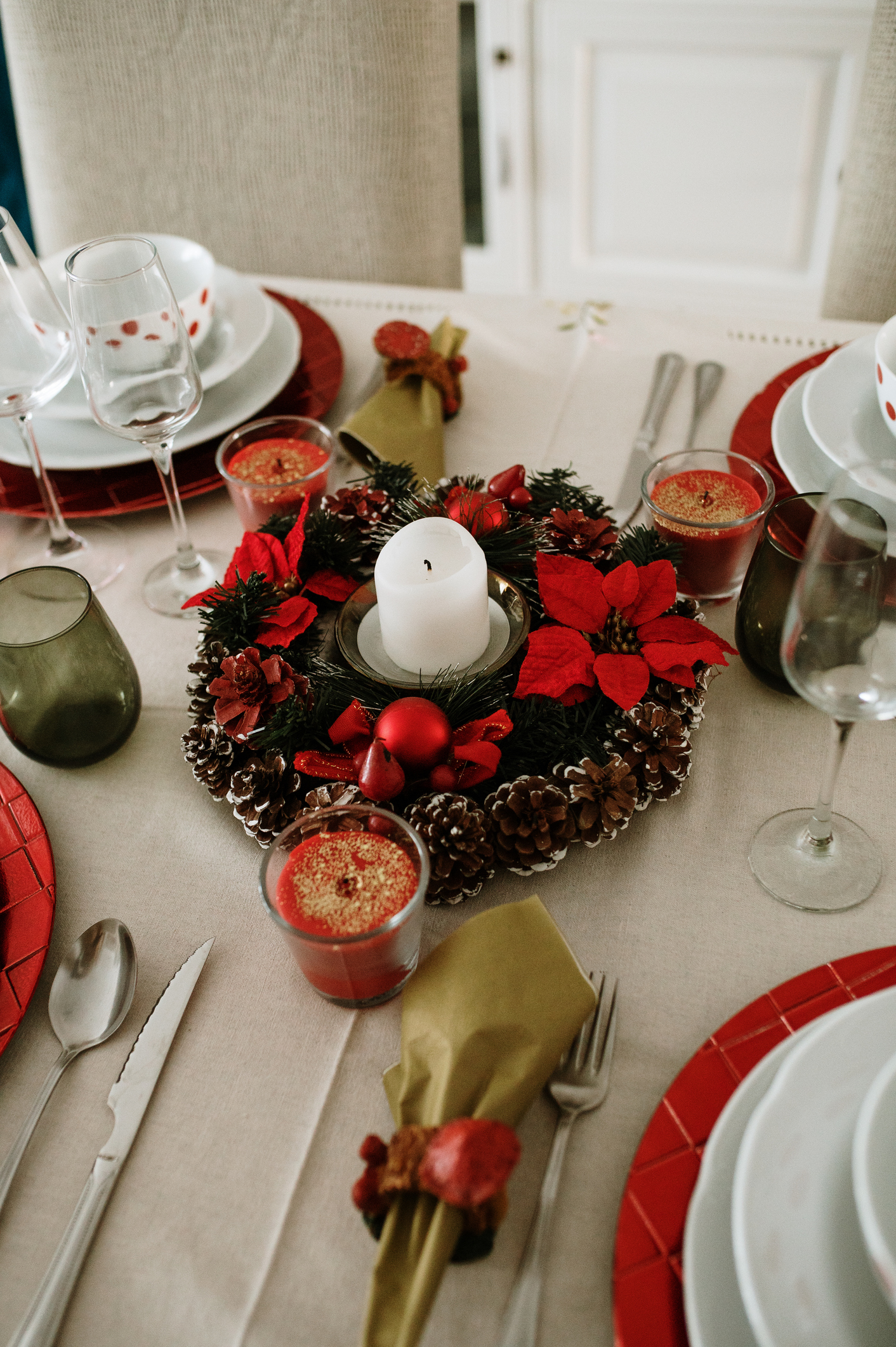 Mesa de Natal com enfeite de centro, vela branca e sousplat vermelho.