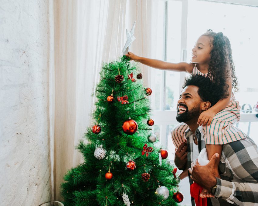 Imagem de pai e filha decorando a árvore de Natal.