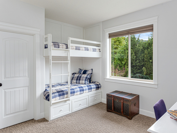 Imagem de um quarto para dois filhos com beliche em madeira branca, baú rústico e roupa de cama xadrez.