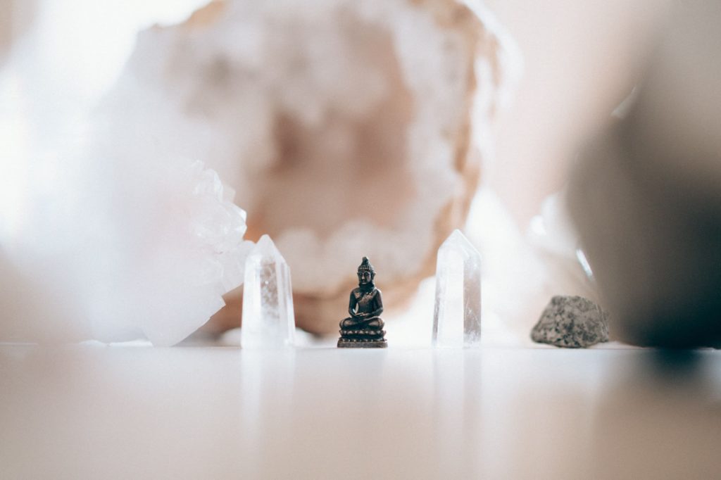 Miniatura de Buda, entre dois cristais brancos. Imagem disponível em Unsplash.