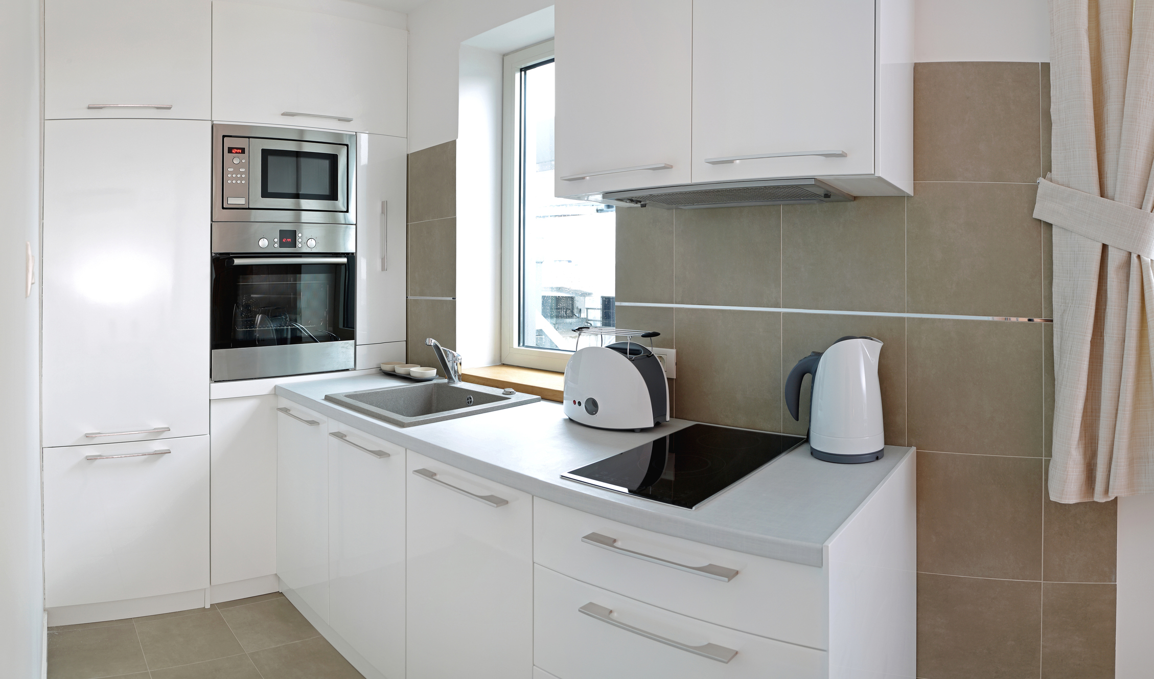 Imagem de uma cozinha toda branca com azulejos cinza na parede.