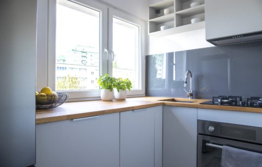 Imagem de uma cozinha pequena com armários em branco e bancada em madeira.