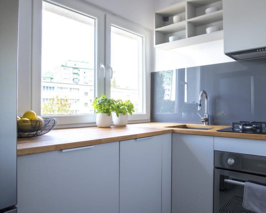Imagem de uma cozinha pequena com armários em branco e bancada em madeira.