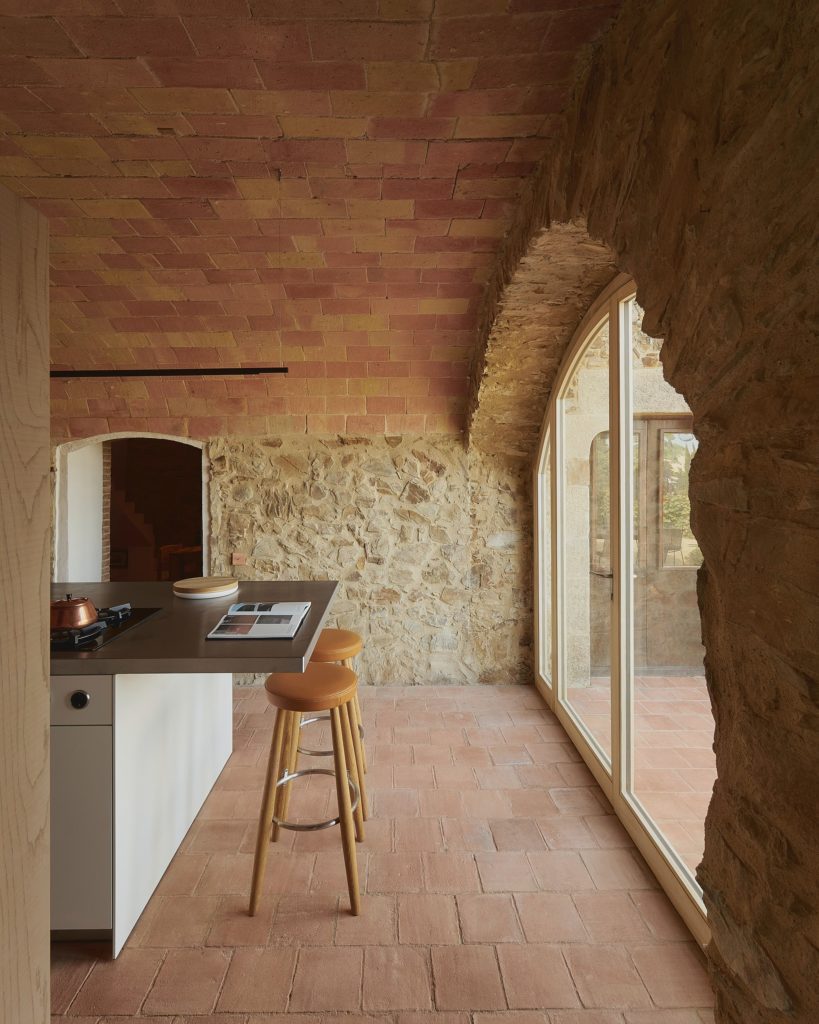 cozinha decorada no estilo grego, com piso e parede feita de pedras. Porta para área externa no formato de arco