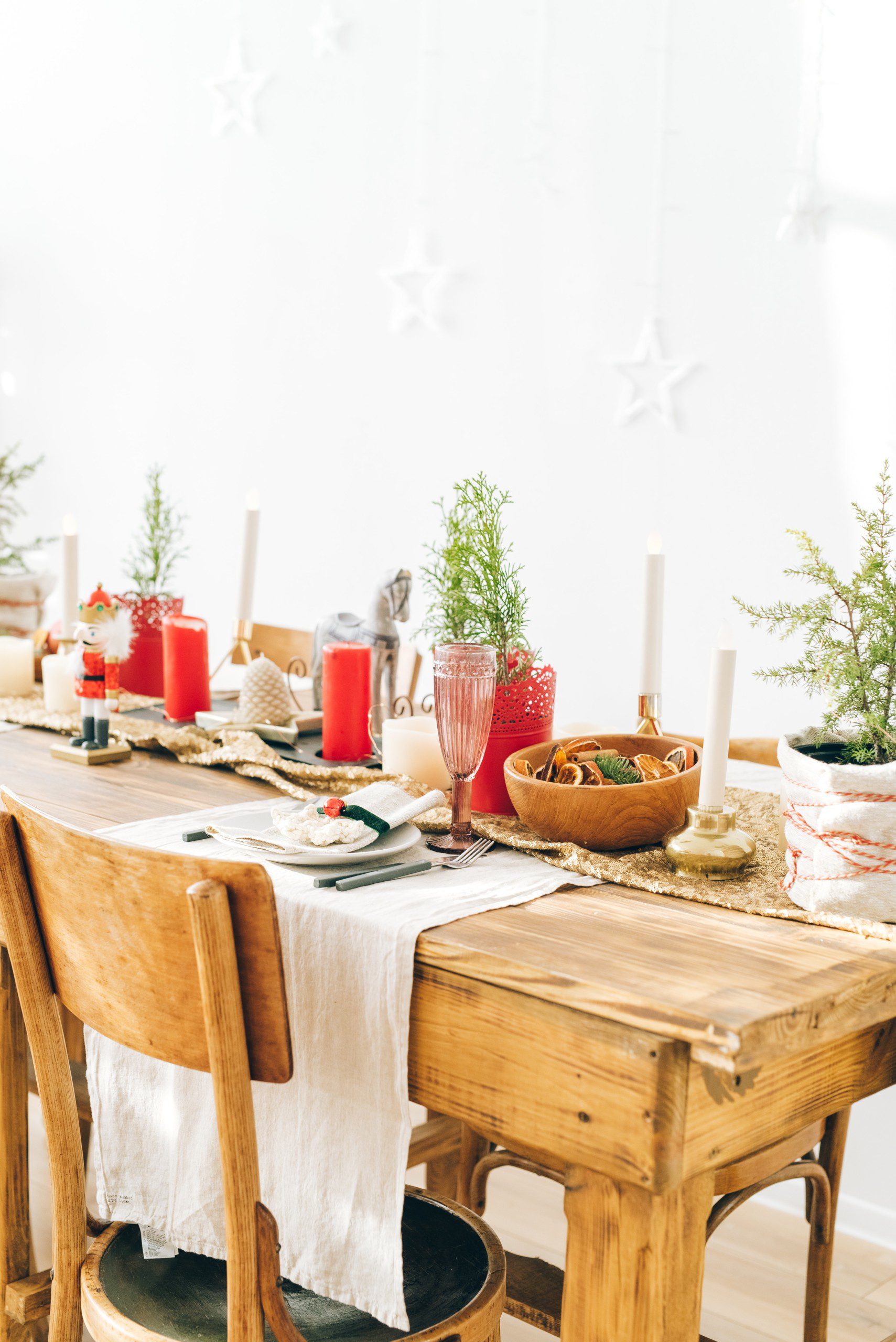 Mesa de Natal com vasos de mini árvores, velas vermelhas e toalha bege.