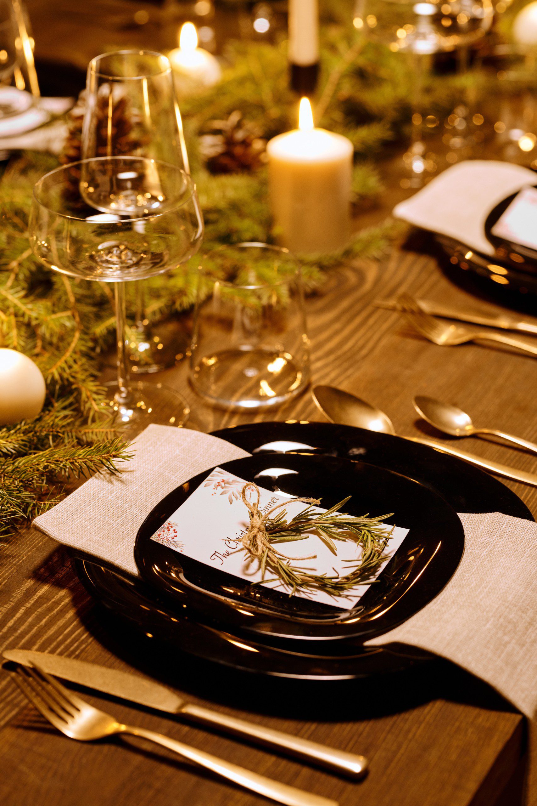 Mesa de Natal com taças de cristal, pratos na cor preta e uma mini guirlanda como enfeite de guardanapo.
