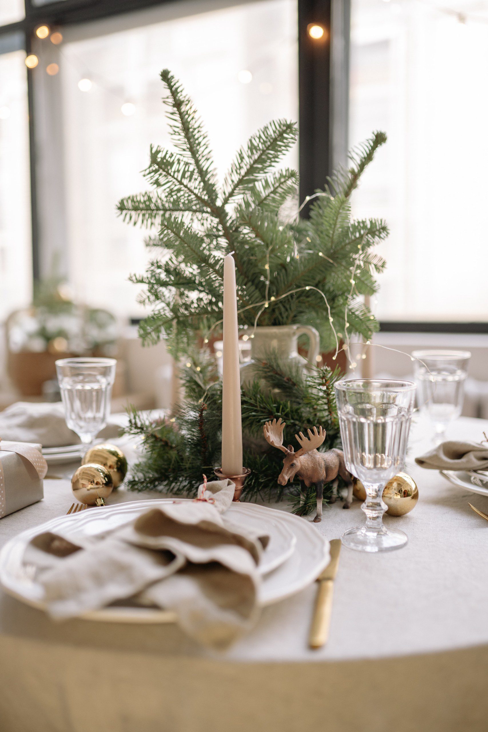 Mesa de Natal clássica com tons claros e um enfeite de centro com uma mini árvore, enfeites e velas.