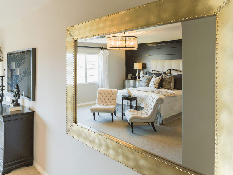 Espelho grande, emoldurado, dá a sensação de amplitude ao quarto de luxo. Imagem disponível em Canva.