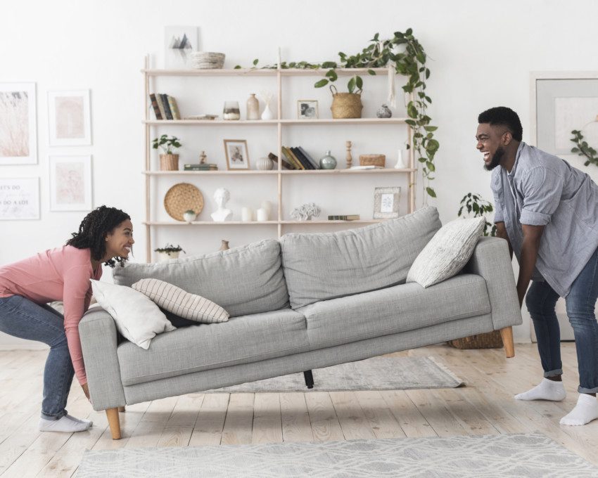 Imagem de uma casal mudando de lugar com sofá de uma sala de estar.