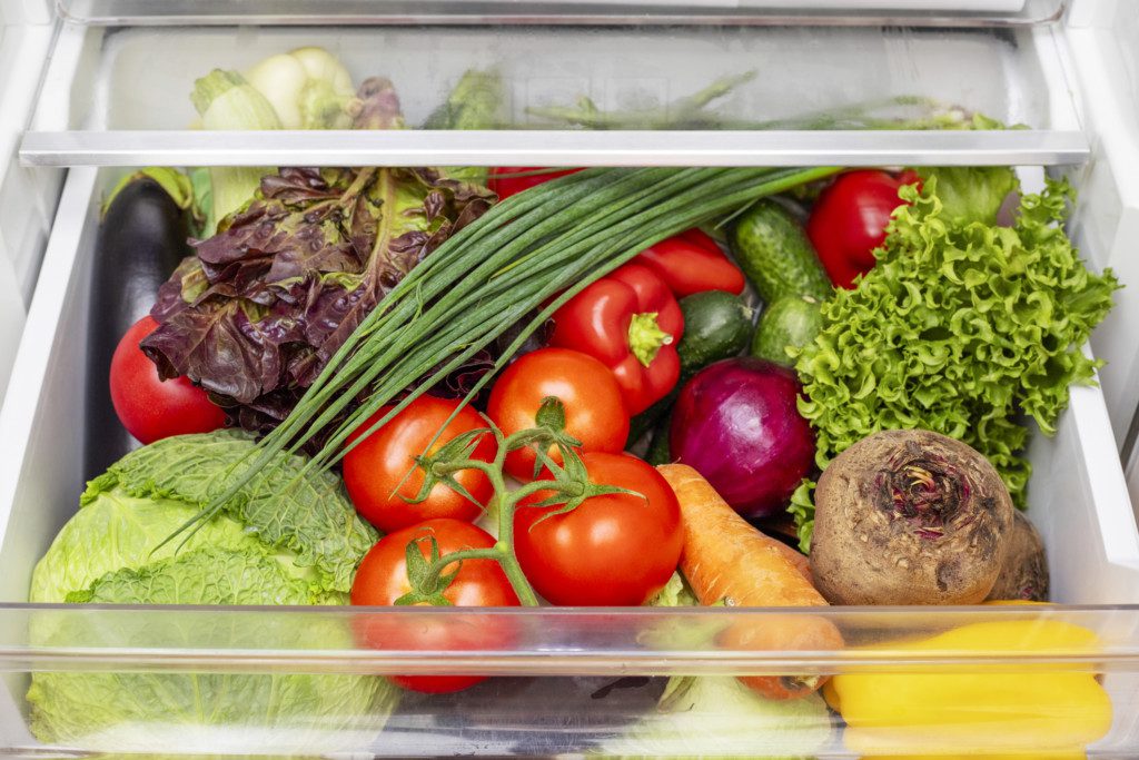 Imagem que ilustra matéria sobre como organizar geladeira mostra uma gaveta da geladeira com legumes e folhagens.