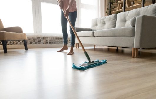 Imagem de uma mulher limpando o chão da casa com um Mop de limpeza.