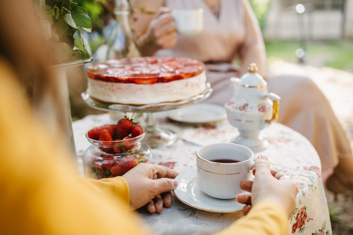 Mesa de uma chá da tarde com xícaras brancas, bule, travessa com morango e uma cheesecake de frutas vermelhas, 