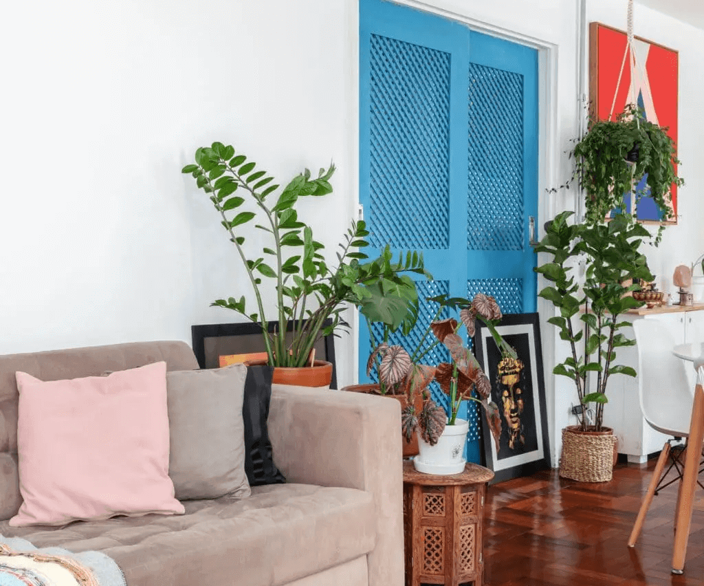Foto que ilustra matéria sobre como decorar a sala gastando pouco mostra uma sala de estar com sofá, plantas e uma grande porta azul em destaque no meio