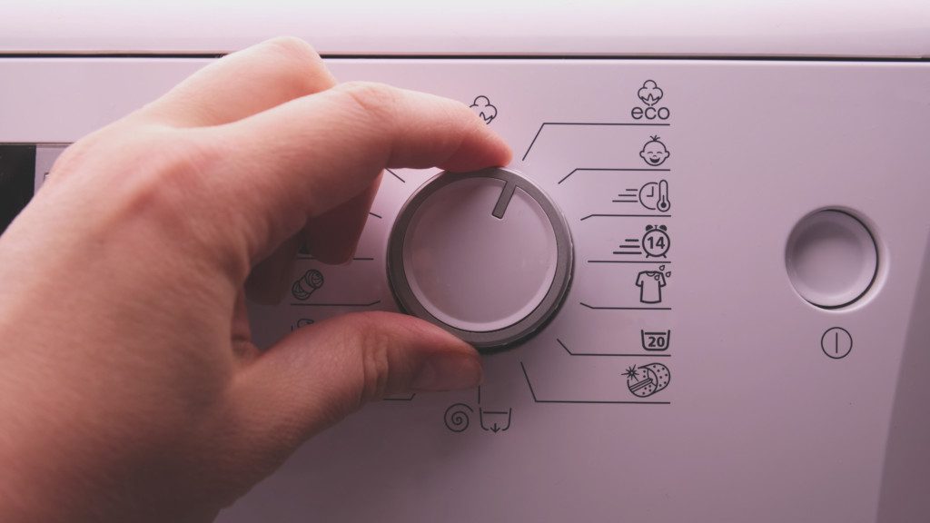 Foto de uma mão configurando programa de economia de água ecológico no painel de controle da máquina de lavar.