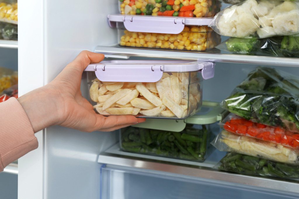Imagem que ilustra matéria sobre como organizar geladeira mostra uma pessoa colocando um pote fechado com batatas congeladas na geladeira.