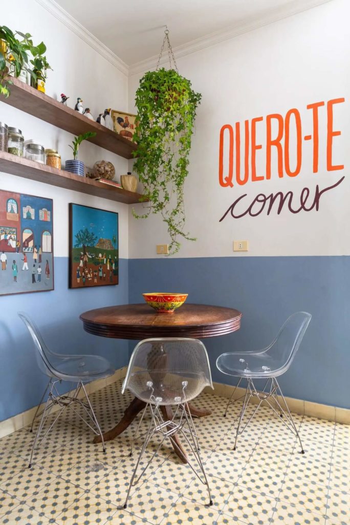 Foto que ilustra matéria sobre pintura setorizada mostra uma cozinha que tem uma área com mesa de jantar delimitada por uma meia parede com metade para cima branca e azul na parte de baixo.