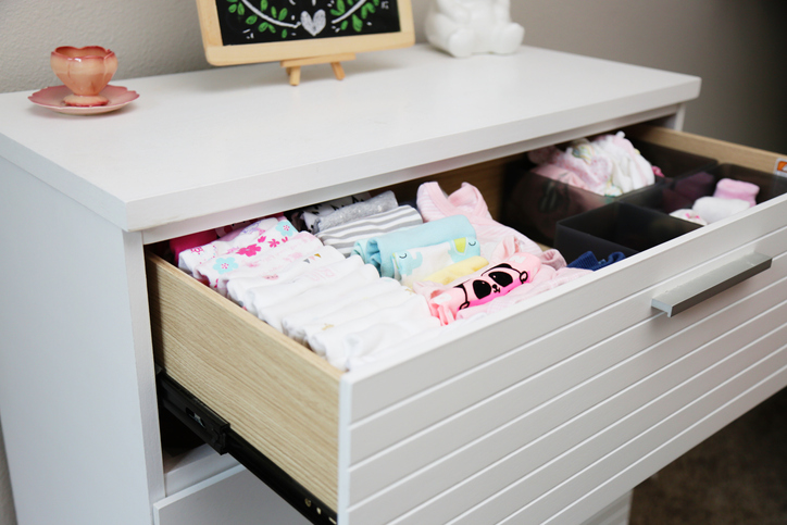 Cômoda branca com a primeira gaveta aberta mostrando a organização de roupas de bebê.