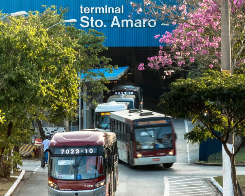 Foto que ilustra matéria sobre o Terminal Santo Amaro mostra diversos ônibus saindo de dentro de dentro do local onde ficam os pontos. Acima deles se vê o letreiro do terminal.