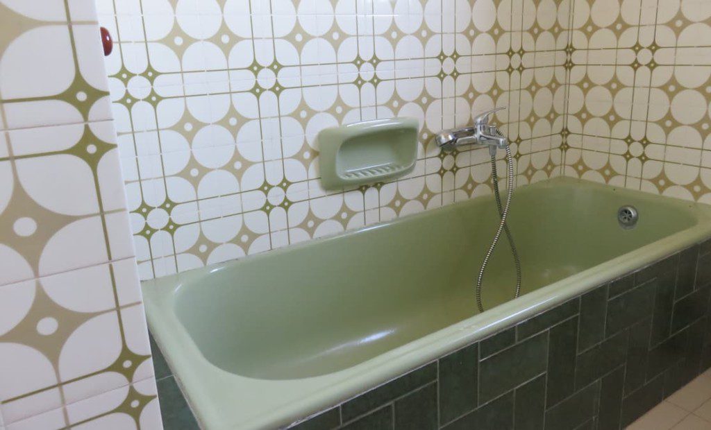 Banheiro retrô revestidos por azulejos em vários tons de verde. Imagem disponível em Getty Images.