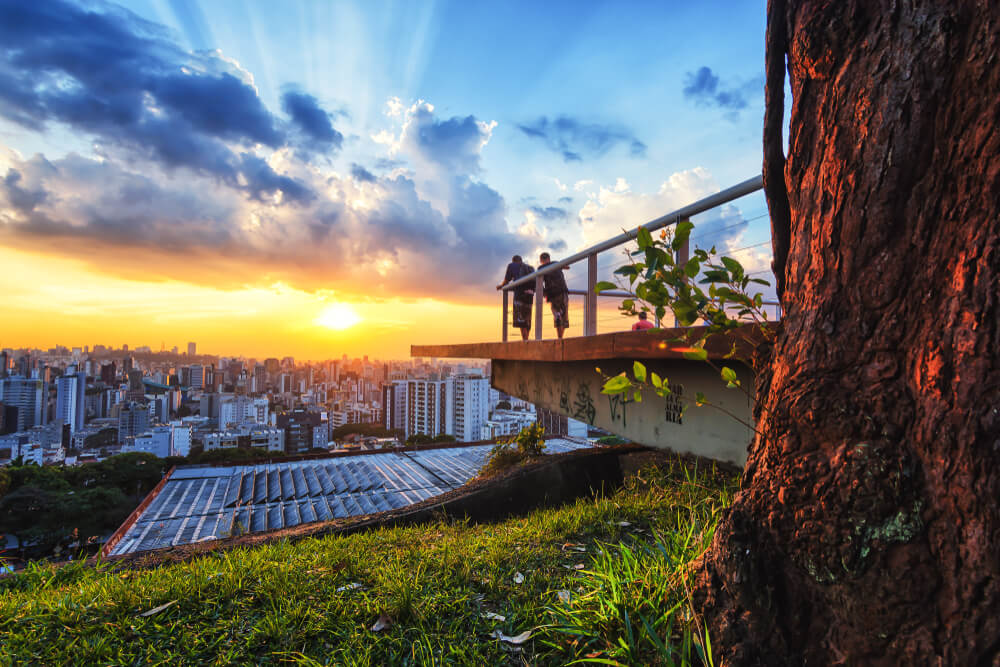  Foto que ilustra matéria sobre os bairros mais seguros de Belo Horizonte mostra a silhueta de dois homens em um deck observando o por do sol na cidade