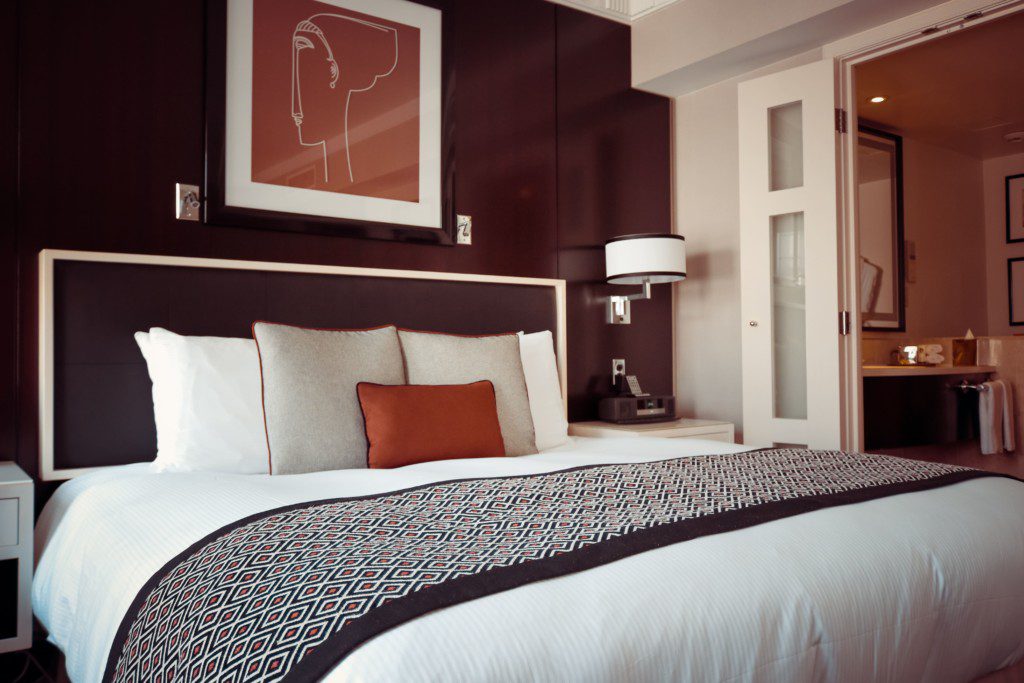 Quarto de casal decorado, com cama posta. Os lençóis combinam com a decorações do quarto, com cores que fazem parte da mesma paleta. Imagem disponível em Pexels.