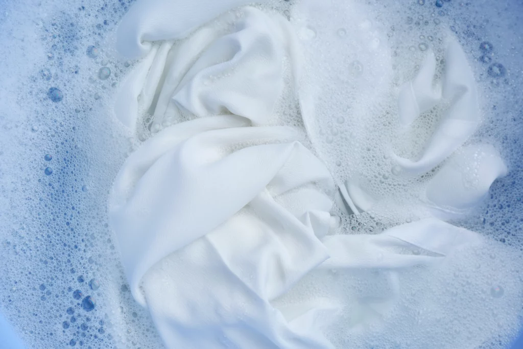 Imagem de roupas brancas imersas em um processo de lavagem com sabão para ilustrar matéria sobre como branquear roupas brancas amareladas