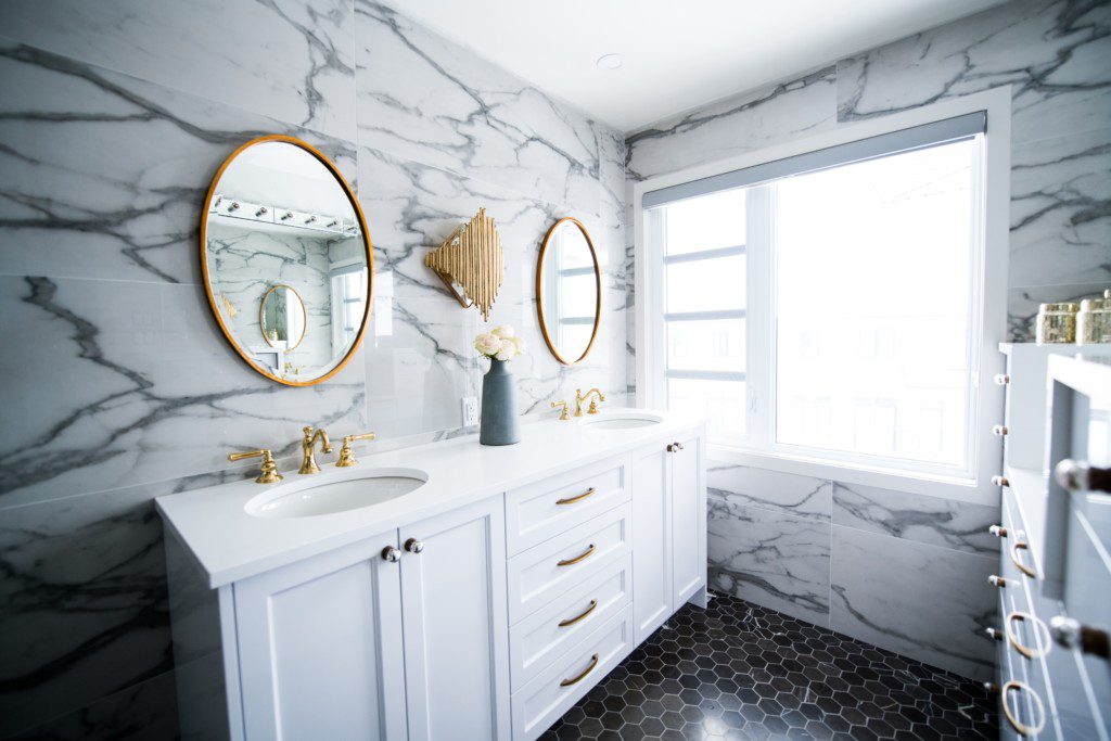 Banheiro com decoração clássica. Paredes revestidas por mármore, detalhes em dourado na moldura do espelho e nas torneiras. Imagem disponível em Unsplash.