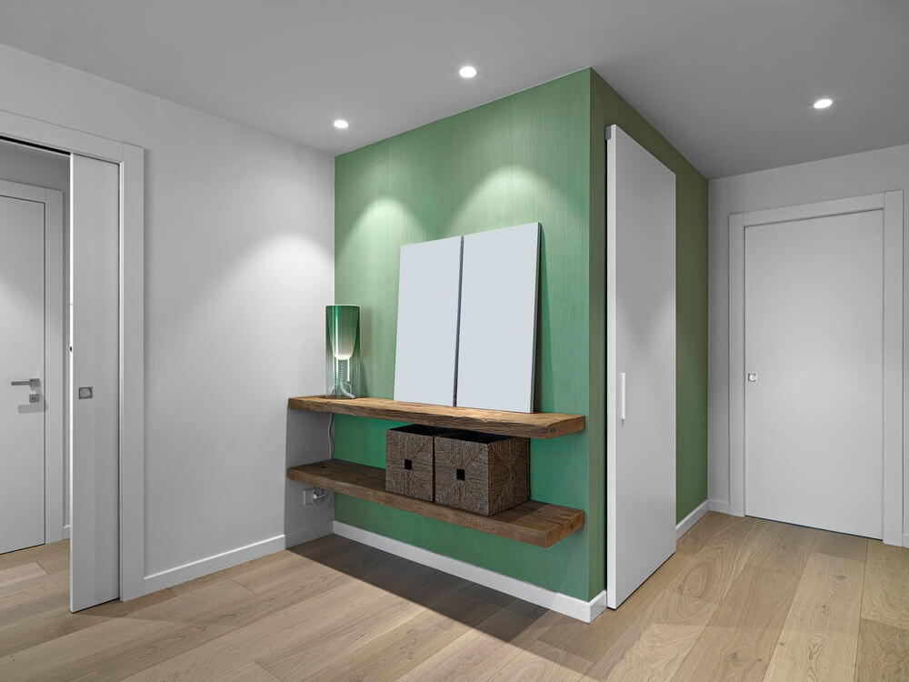 Foto que ilustra matéria sobre como decorar a sala gastando pouco mostra o hall de entrada de um apartamento com duas paredes pintadas de verde, contrastando com outra parede e portas brancas
