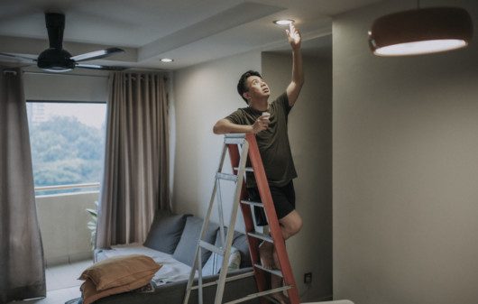 Imagem de um homem em cima de uma escada trocando a lâmpada.