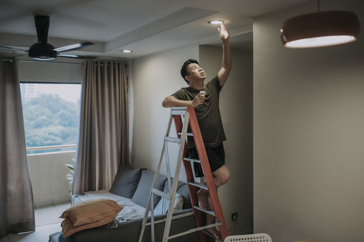Imagem de um homem em cima de uma escada trocando a lâmpada.