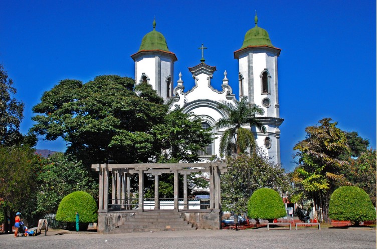  Foto que ilustra matéria sobre os bairros mais seguros de Belo Horizonte mostra a praça Duque de Caxias com a Igreja Santa Tereza, com sua fachada branca e cúpulas verdes ao fundo em um dia de céu azul