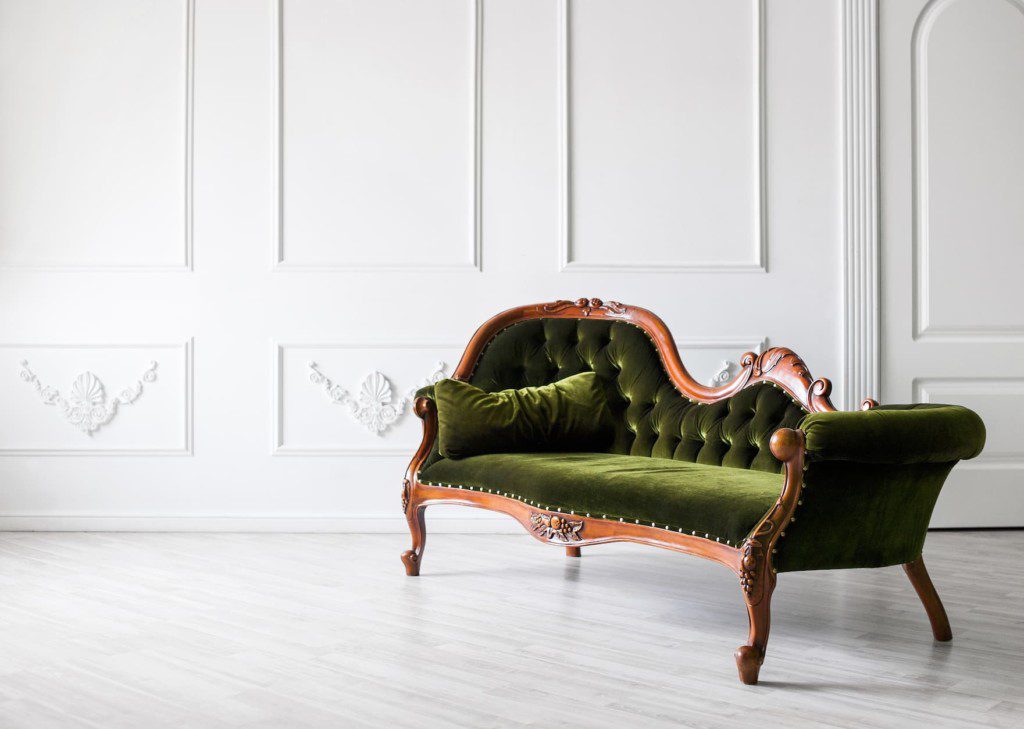 Sofá de madeira ao lado de parede branca com molduras de gesso. Imagem disponível em Getty images.