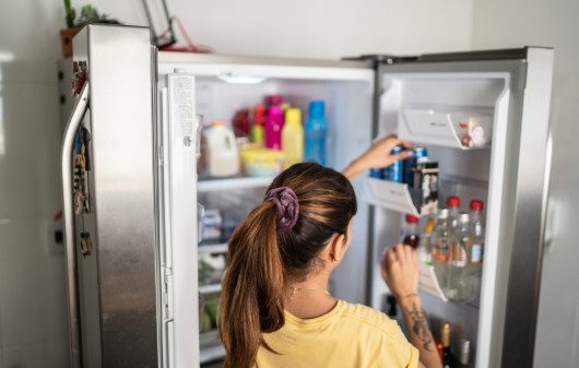 Imagem que ilustra matéria sobre como organizar geladeira mostra uma mulher colocando uma latinha de refrigerante na porta de sua geladeira.