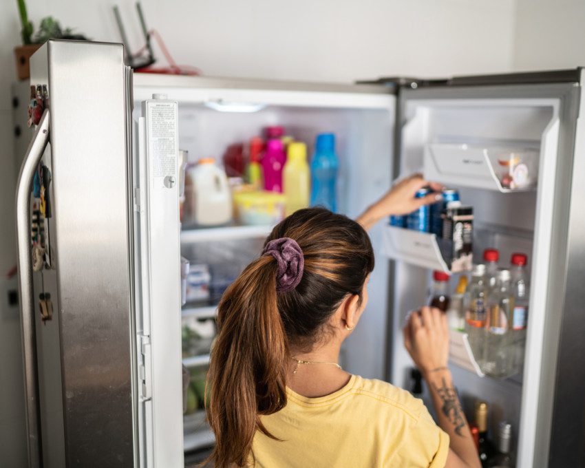 Imagem que ilustra matéria sobre como organizar geladeira mostra uma mulher colocando uma latinha de refrigerante na porta de sua geladeira.