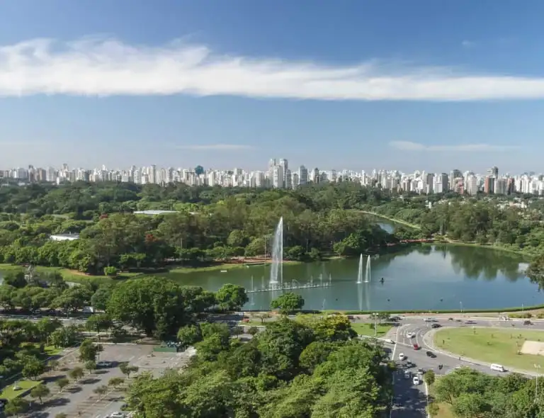 Imagem da vista aérea do Parque Ibirapuera mostra vegetação, lago e prédios ao fundo para ilustrar matéria sobre parques gratuitos em SP