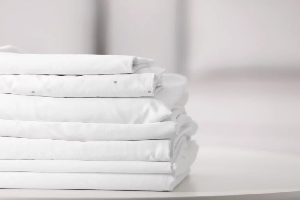 Imagem de roupas de cama brancas limpas e dobradas na mesa de centro de uma casa para ilustrar matéria sobre roupa branca, como clarear?
