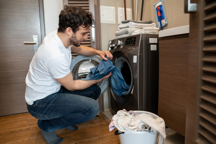 Homem colocando roupas para lavar na máquina.