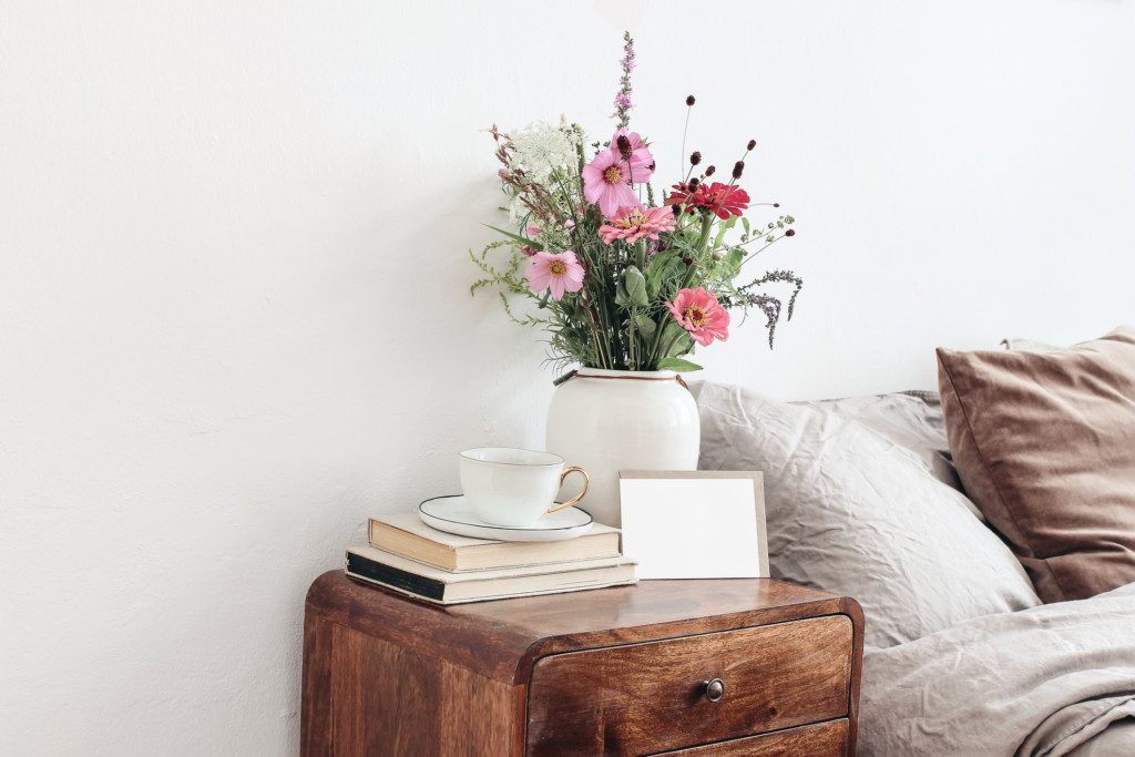 Mesa de cabeceira rústica em madeira, com livro, vaso de flores e porta retrato.
