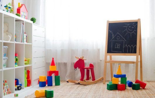 Imagem que ilustra matéria sobre quarto de brinquedos mostra um quarto de brinquedos com tapete, brinquedos no chão e cômoda e quadrinhos decorativos