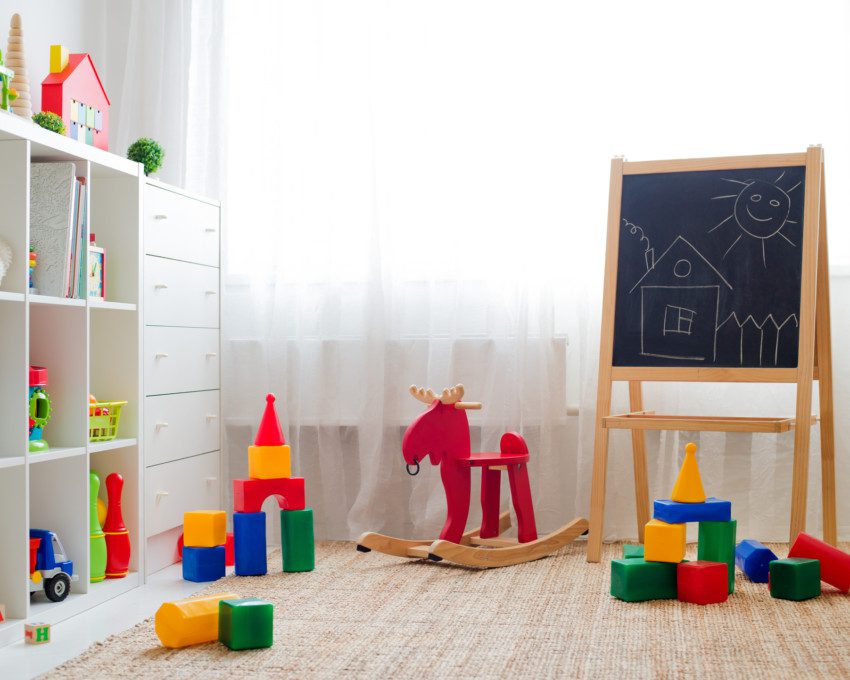 Imagem que ilustra matéria sobre quarto de brinquedos mostra um quarto de brinquedos com tapete, brinquedos no chão e cômoda e quadrinhos decorativos