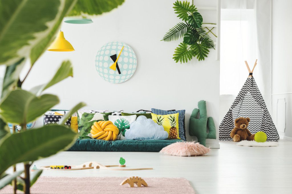  Imagem que ilustra matéria sobre quarto de brinquedos mostra um quarto de brinquedos com tapete, brinquedos no chão, sofá e cabaninha
