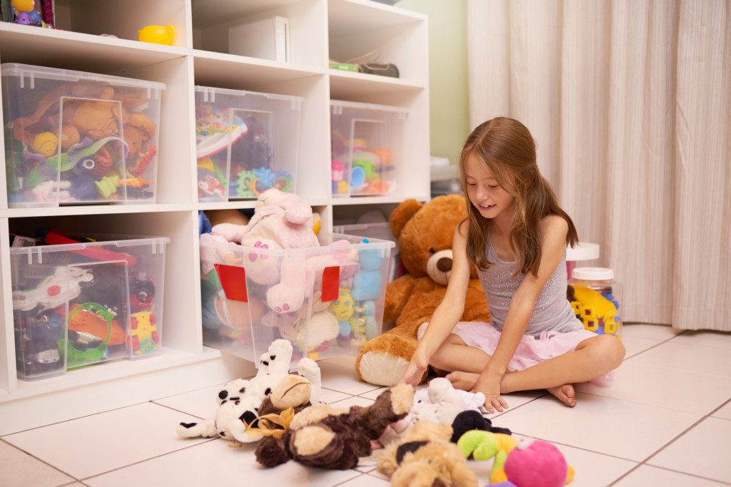 Imagem que ilustra matéria sobre quarto de brinquedos mostra um quarto de brinquedos com vários cestos de brinquedos e uma criança sentada no chão
