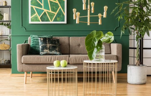 Sala de estar com parede verde, detalhes em aramado dourado e plantas.