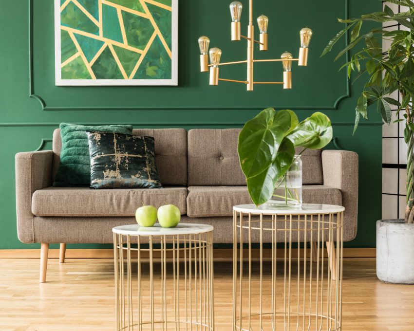 Sala de estar com parede verde, detalhes em aramado dourado e plantas.