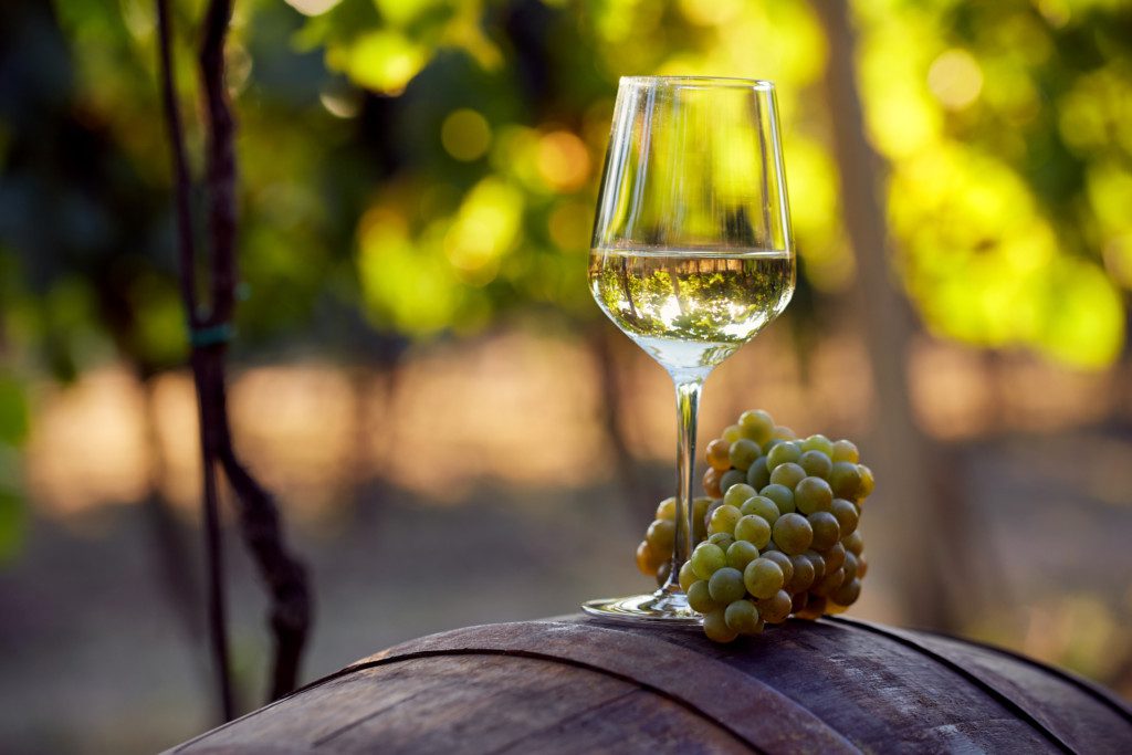 Taça de vinho branco encima de um barril com um cacho de uvas.