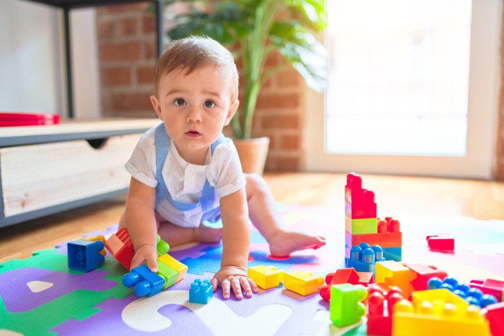 Imagem que ilustra matéria sobre quarto de brinquedos mostra um quarto de brinquedos com tapete educativo e brinquedos educativos com um bebê sentado